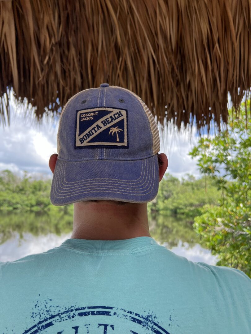 A man wearing a blue hat standing under an umbrella.