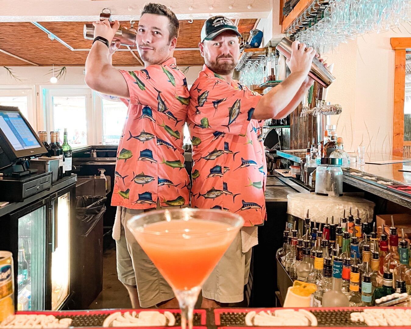 Two men standing in front of a bar with a drink.