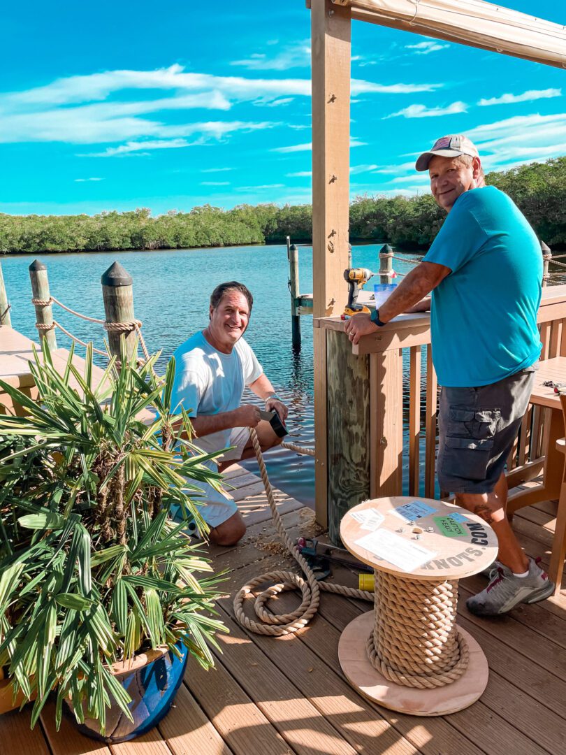 Two men are sitting on a deck near the water.