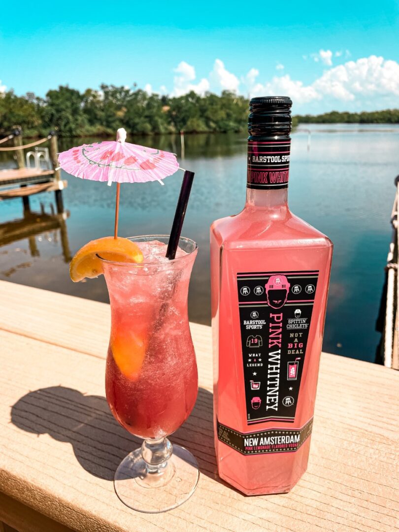 A bottle of pink lemonade and a glass on the deck.