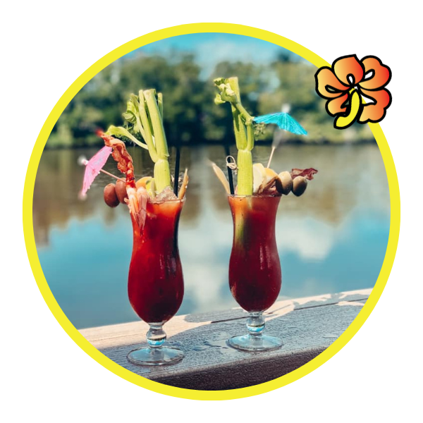 Two glasses of drink with a flower and water in the background.