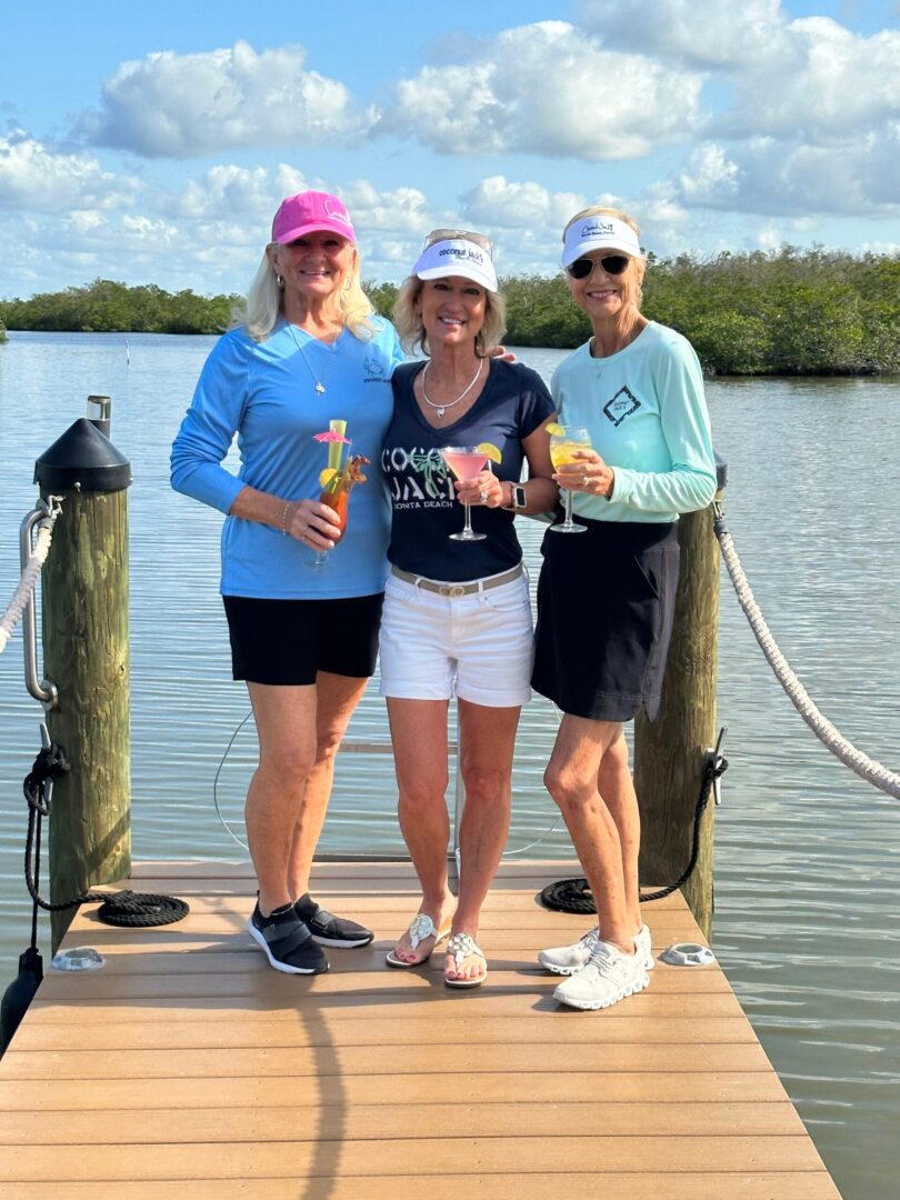 Three women standing on a dock holding drinks.