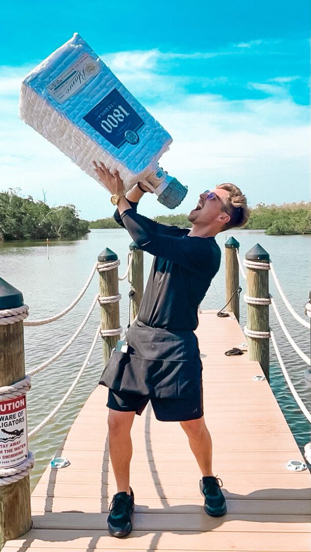 A man holding up a bottle of water on the dock.